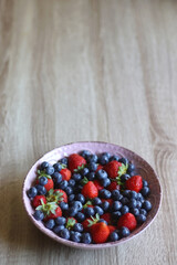 Pink rustic bowl filled with fresh blueberries and strawberries. Wooden background, selective focus.