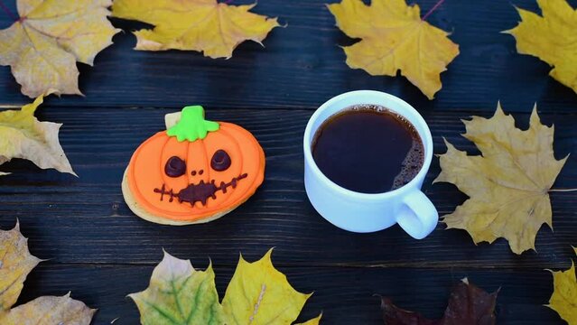 Pumpkin cookie and cup of coffee on wooden table strewn with autumn leaves. Concept of Halloween holiday. Close up