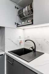 Black shell and matte black crane located on white surfaces of porcelain plates that imitate the appearance of natural stones. Open cabinet with dishes