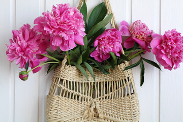 pink peonies in a wicker bag on the wall, close-up.
