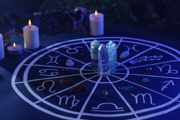 Natural stones for zodiac signs, drawn astrology chart and burning candles on dark blue table