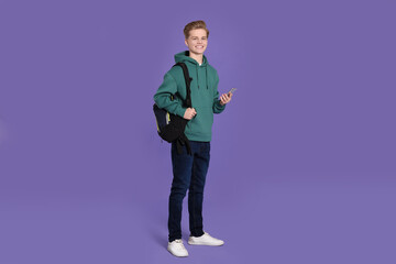 Teenage boy with backpack using smartphone on purple background