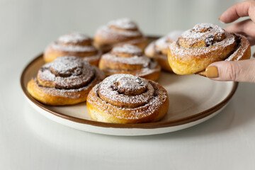 Freshly baked cinnamon rolls sprinkled with powdered sugar on parchment paper. Sweet homemade Christmas baking. . Kanelbule is a Swedish dessert.