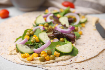 Tortilla with hummus and vegetables on table, closeup