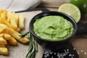 Serving board with french fries, avocado dip, rosemary and lime served on wooden table, closeup
