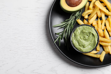 Plate with french fries, guacamole dip, rosemary and avocado served on white wooden table, top view. Space for text