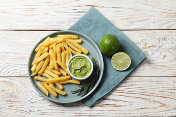 Plate with delicious french fries, avocado dip, lime and rosemary served on white wooden table, top view