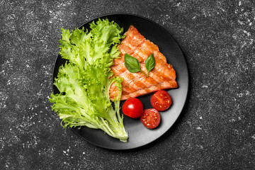 Tasty grilled salmon with tomatoes and fresh lettuce on black table, top view