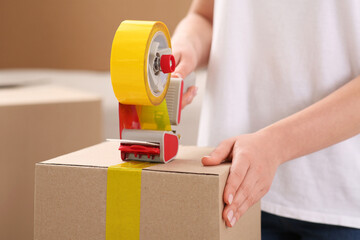 Woman applying adhesive tape on box with dispenser indoors, closeup