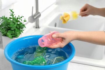 Woman washing baby bottle in kitchen, closeup