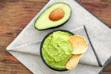 Delicious guacamole made of avocados with nachos and cut fruit on wooden table, flat lay