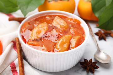 Bowl of tasty persimmon jam and ingredients on white marble table, closeup