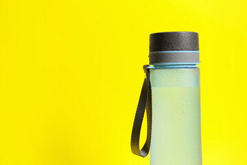 Stylish closed bottle with water drops on yellow background, closeup. Space for text