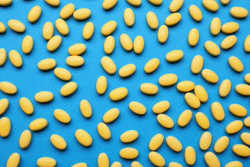 Many yellow dragee candies on blue background, flat lay