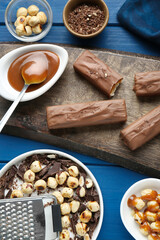 Tasty chocolate bars with caramel and nuts on light blue wooden table, flat lay