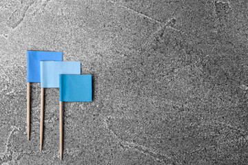 Small light blue paper flags on grey background, flat lay. Space for text