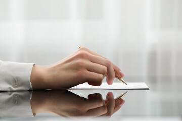 Woman writing on sheet of paper at glass table, closeup