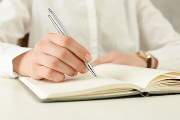 Woman writing in notebook at white table, closeup - obrazy, fototapety, plakaty