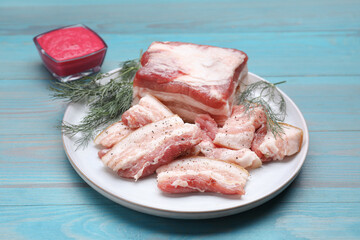 Pieces of pork fatback with dill and sauce on light blue wooden table