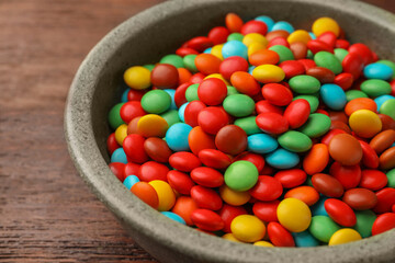 Bowl with tasty colorful candies on wooden table, closeup