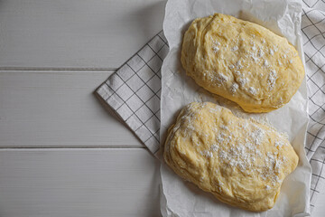 Raw dough and flour on white wooden table, top view with space for text. Cooking ciabatta
