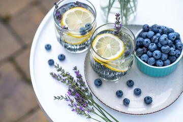Two glasses with homemade lemonade made of fresh blueberries, lemon and lavender on white round table on backyard in summer day.