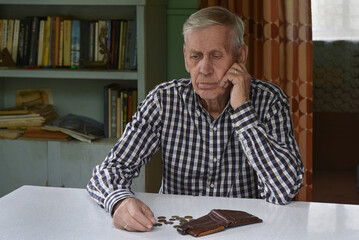 Sad old man sits at the table, looks at the money and wallet.  The concept of poverty, low income, austerity in old age.	