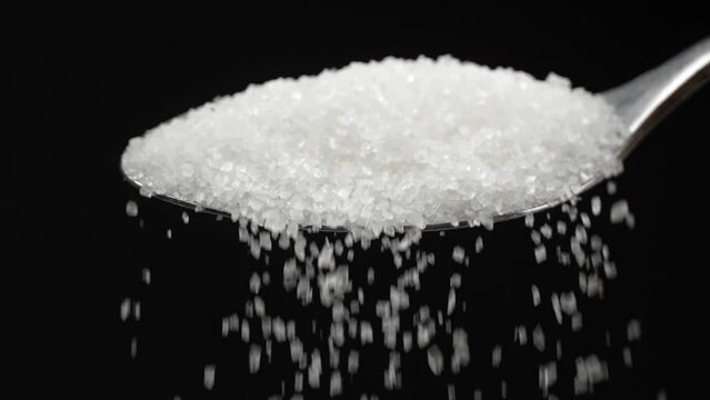 Sugar spoon full of powdered sugar crystals in teaspoon side view, filled with sugar for cooking and baking needed for drinks - coffee or tea is poured in slow motion close-up.