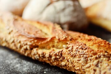 Bakery products in a wicker basket. Round homemade bread, long loaf with seeds, vegan bread without yeast. Wooden background