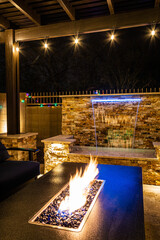 A resort style backyard at night with a waterfall, pergola, and a firepit at night.