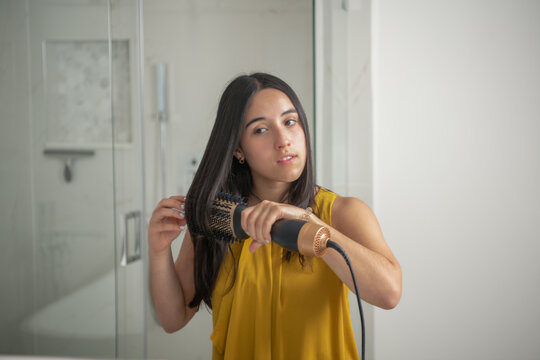young woman using a modern rotative hair brush to style her hair.