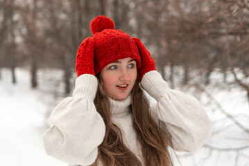 Portrait of beautiful young woman in knitted red hat and mittens and woolen sweater in winter park. Ladies knitwear