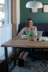 Young caucasian woman sitting in cafe alone with white cup of tea coffee latte and wait someone. Vertical frame.