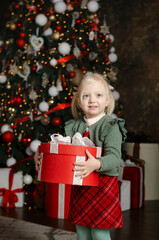 Fototapeta na wymiar Happy little girl holds large big gift box and looks into camera on xmas tree background. Christmas Eve. Vertical frame.