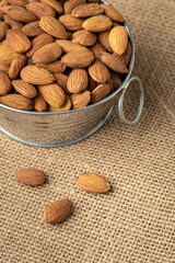 Metal bowl full of almonds on a sackcloth. Pile of nuts stacked together randomly on the burlap background. Healthy nutrition concept