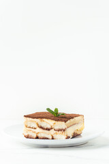 Homemade tiramisu cake on white plate against white background. Traditional Italian no-bake dessert made of savoiardi, filled with mascarpone cheese, coffee espresso and sprinkled with cocoa powder