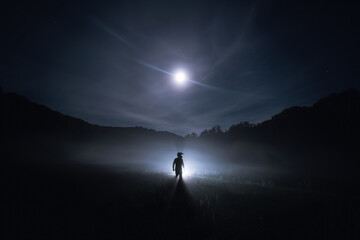 Silhouette of Motorcyclist, biker in a helmet standing in the dark field with light. Horror...