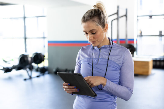 Caucasian fit woman standing using tablet at fitness gym