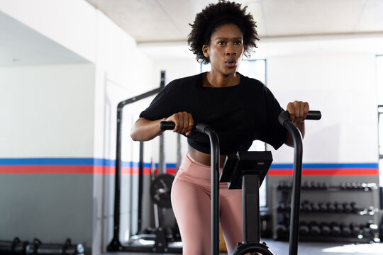 African american fit woman exercising and using cross trainer at gym