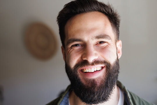 Close-up portrait of handsome bearded biracial young man smiling against white wall, copy space