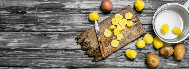 Fototapeta na wymiar Sliced potatoes on a cutting Board with a knife and peeled potatoes in a saucepan.