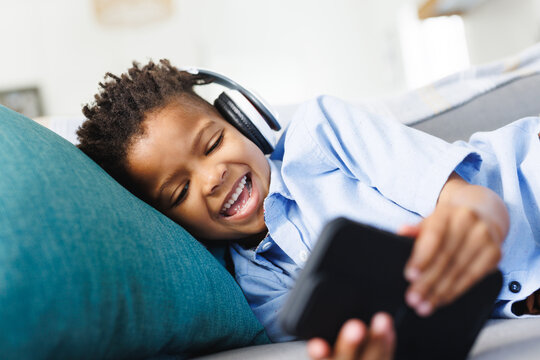 Happy african american boy sitting on sofa, using smartphone in living room