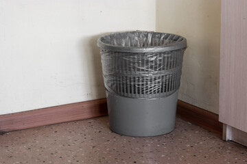 Gray plastic waste paper basket with black transparent rubbish bag inside at the office corner - 561128154