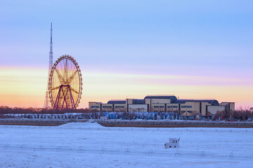 Ferris wheel and TV tower on the bank of a snow-covered river on a winter morning. Sunrise at the International Border between China and Russia