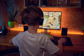 Hands of teenage gamer boy playing video games on computer in dark room using backlit colorful keyboard