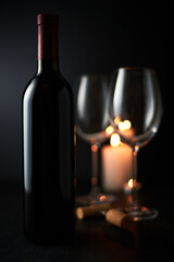 expensive bottle of wine and a glass with red wine on a dark glossy background.