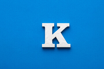Alphabet letter K - White wooden letter on blue foamy background