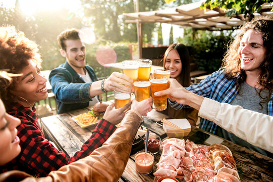 Young multiracial people drinking beer at brewery bar out doors - Happy family having barbecue party in backyard restaurant patio - Concept about friends enjoying time  together - Focus on pint glass