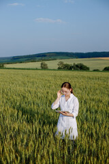 Scientist technologist in a white coat on a young wheat field writes down data on this year's crop on a smart tablet