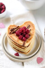 Heart-shaped pancakes lie on top of each other, with chocolate and raspberries on top. Breakfast for Valentine's Day with love.
